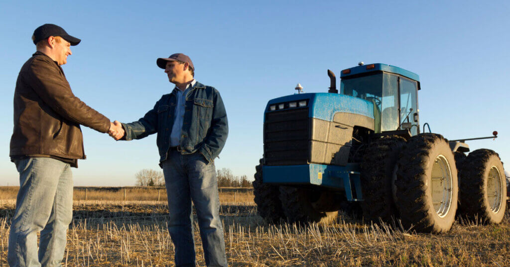 two farmers shaking hands on a field near a tractor