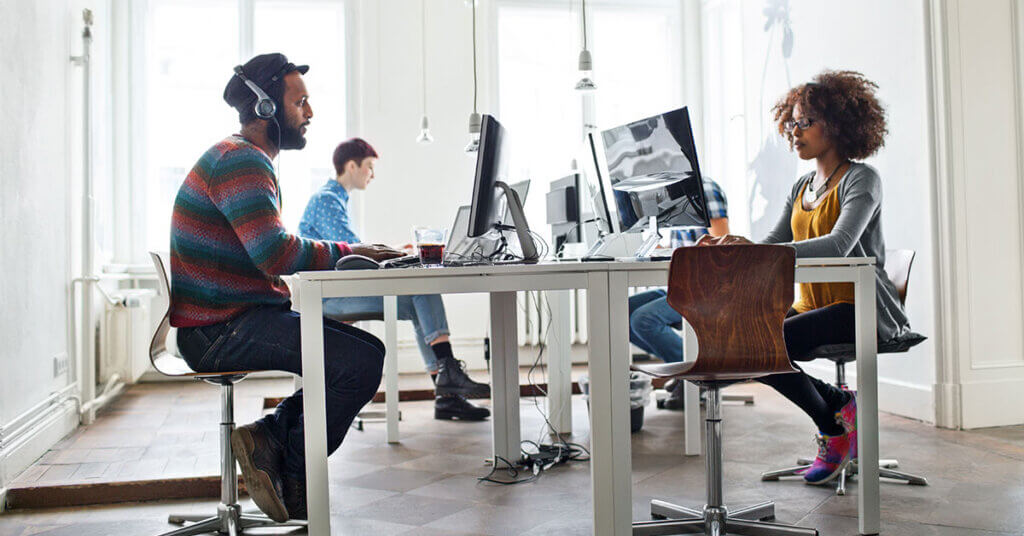 Four coworkers at their desks working on their individual workstations.