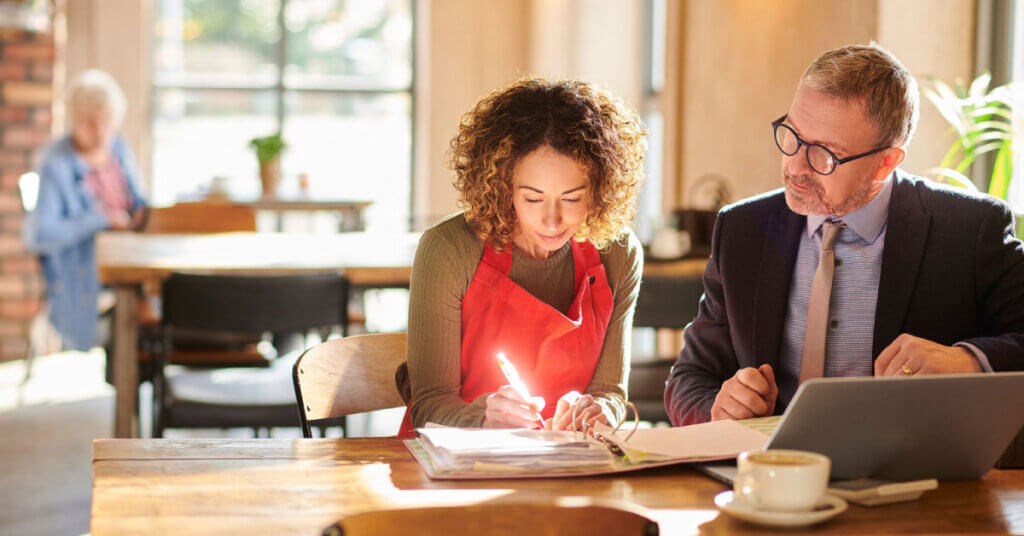 small business owner and commercial lender go over paperwork in a coffee shop