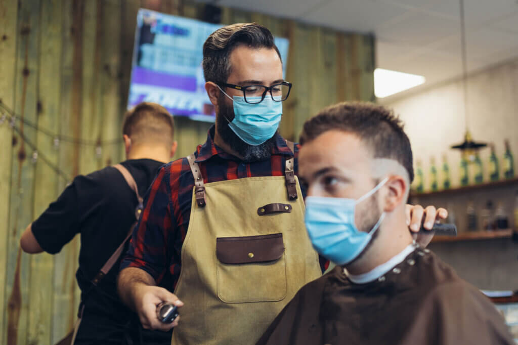 Young man wearing a mask gets his hair cut at a barbershop.
