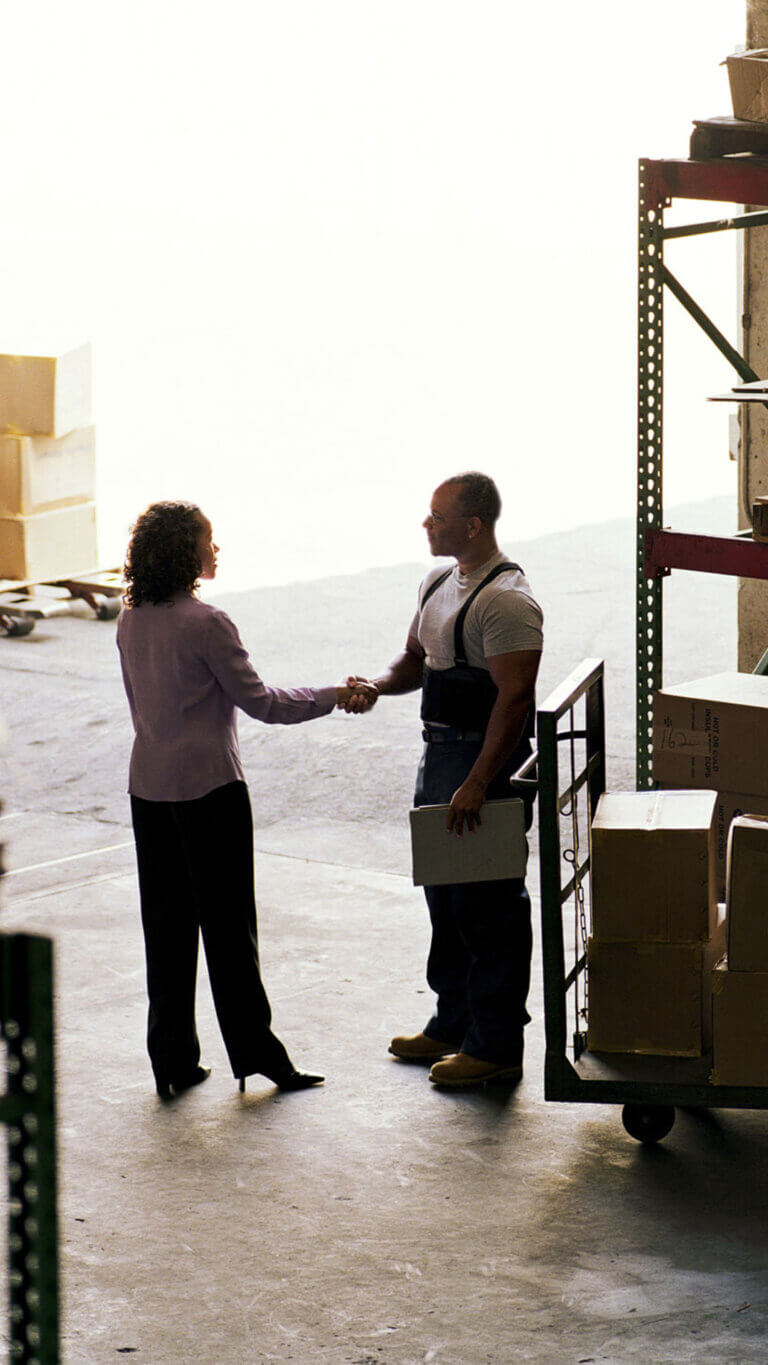 Warehouse manager and female office colleague shaking hands in warehouse.