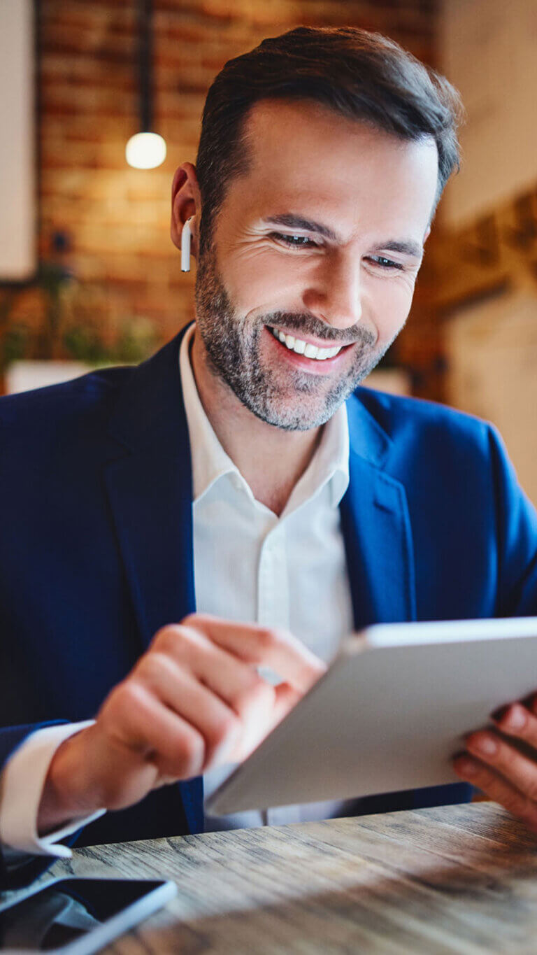 Businessman on his tablet working remotely, listening to air pods.