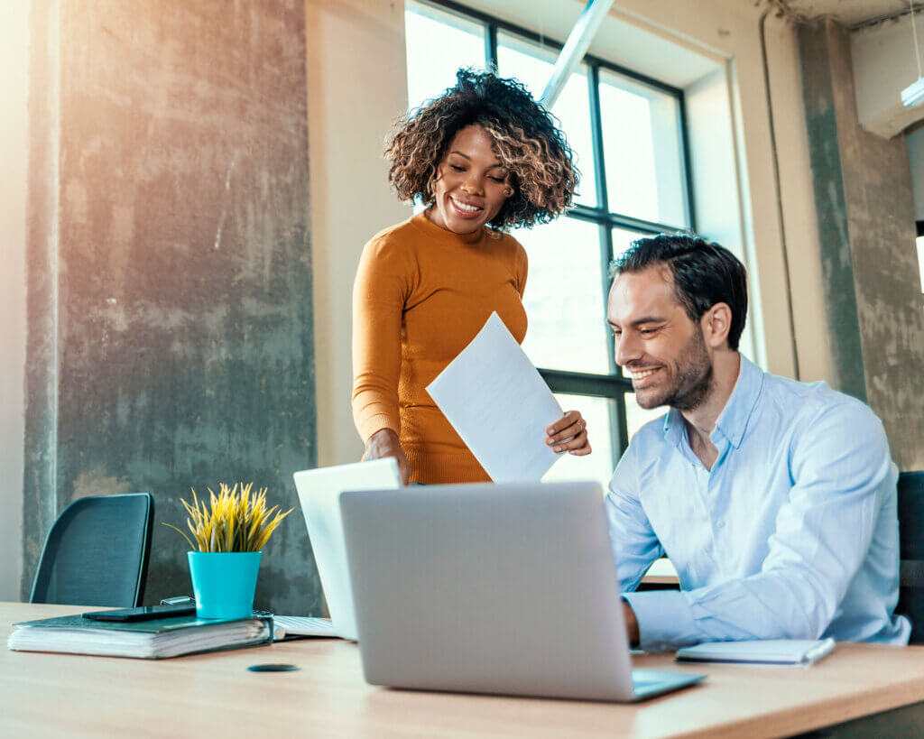 Young woman looking over male colleagues shoulder at laptop in an industrial office.