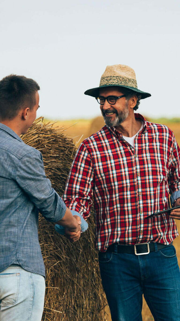 Two farmers shaking hands over business deal made in the hay field.