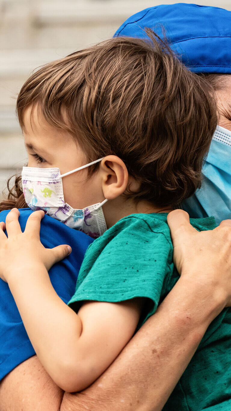 Healthcare worker embraces a child, both with masks on.