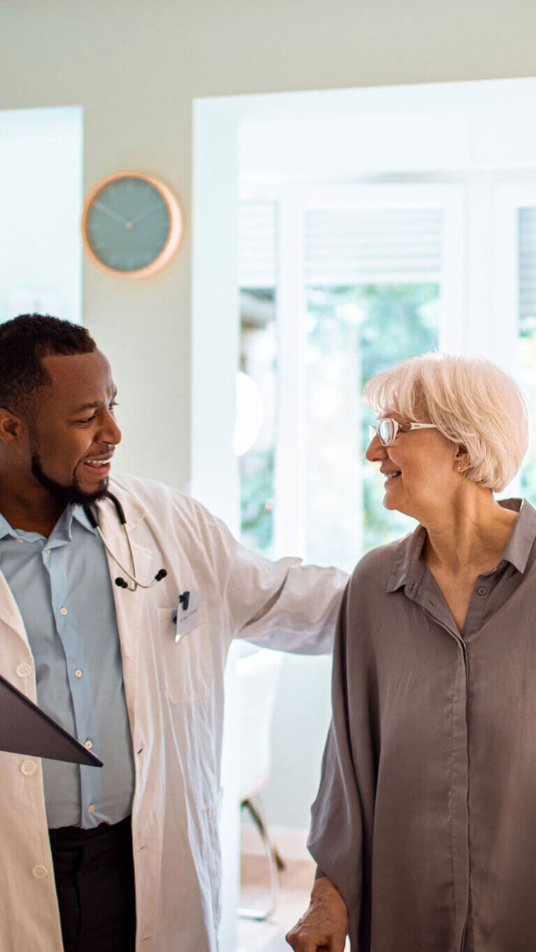 Male healthcare worker in white lab coat examining a senior woman at a doctors appointment.