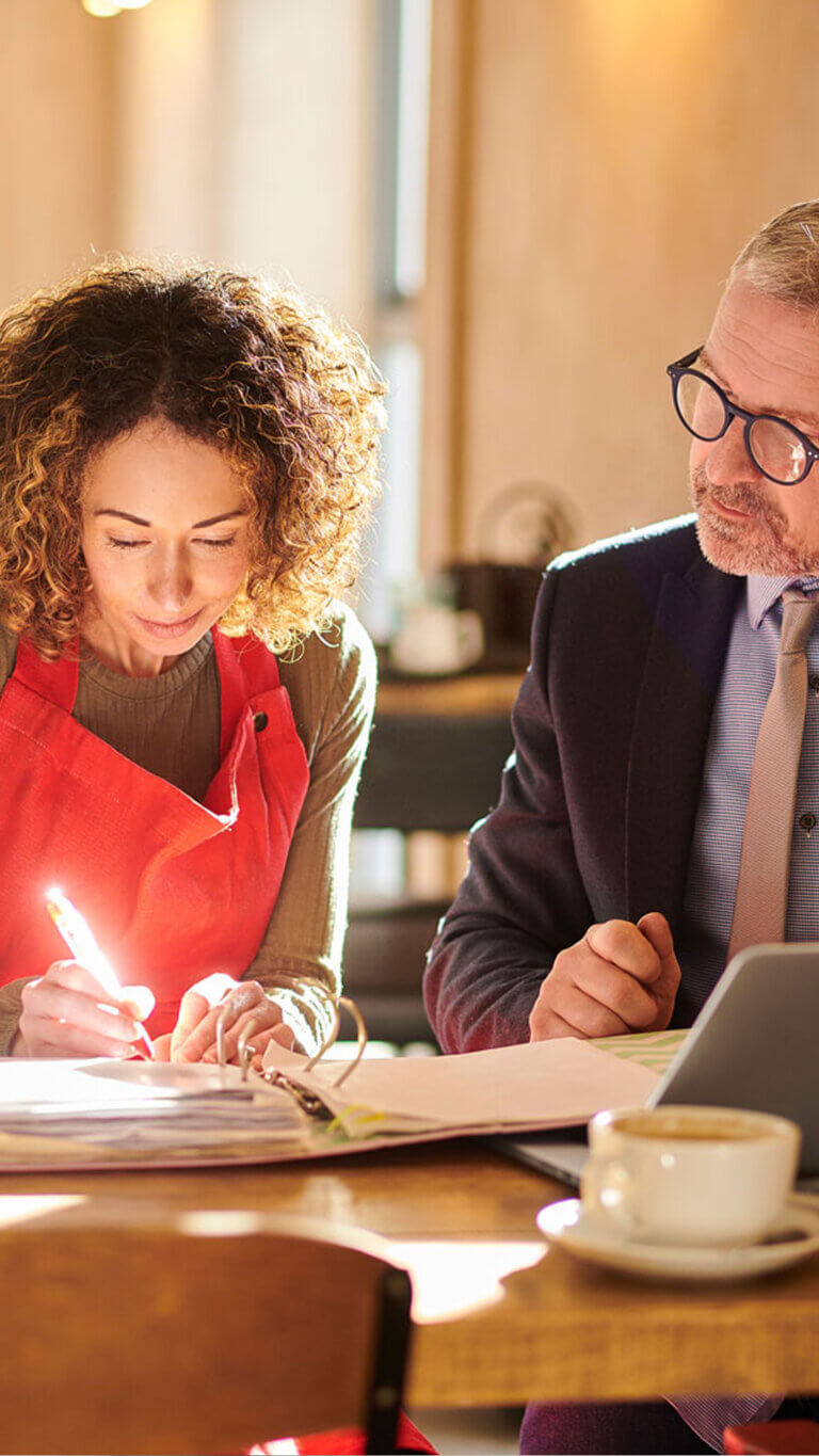Small business owner with commercial loan specialist reviewing loan details in a coffee shop setting.