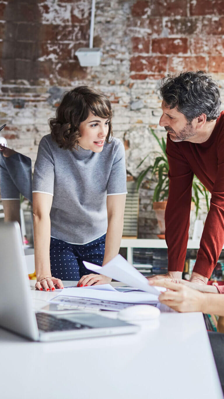 Small business colleagues discussing commercial loans over desk and laptop.