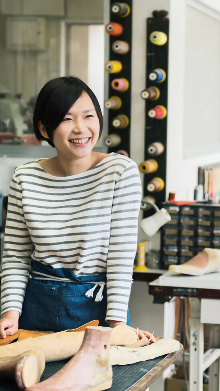 Small business shoe designer standing at drafting table and smiling.