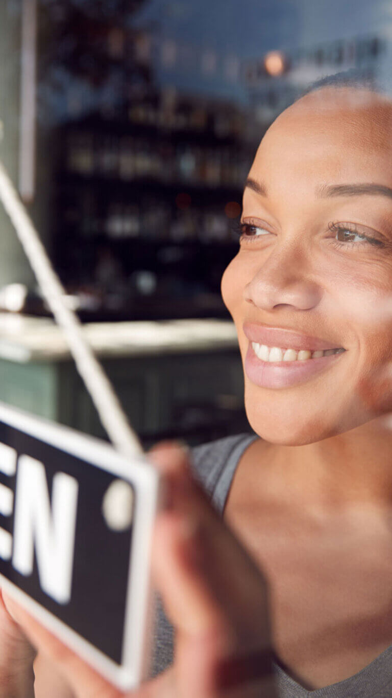 Happy small business owner turning her door sign to Open.