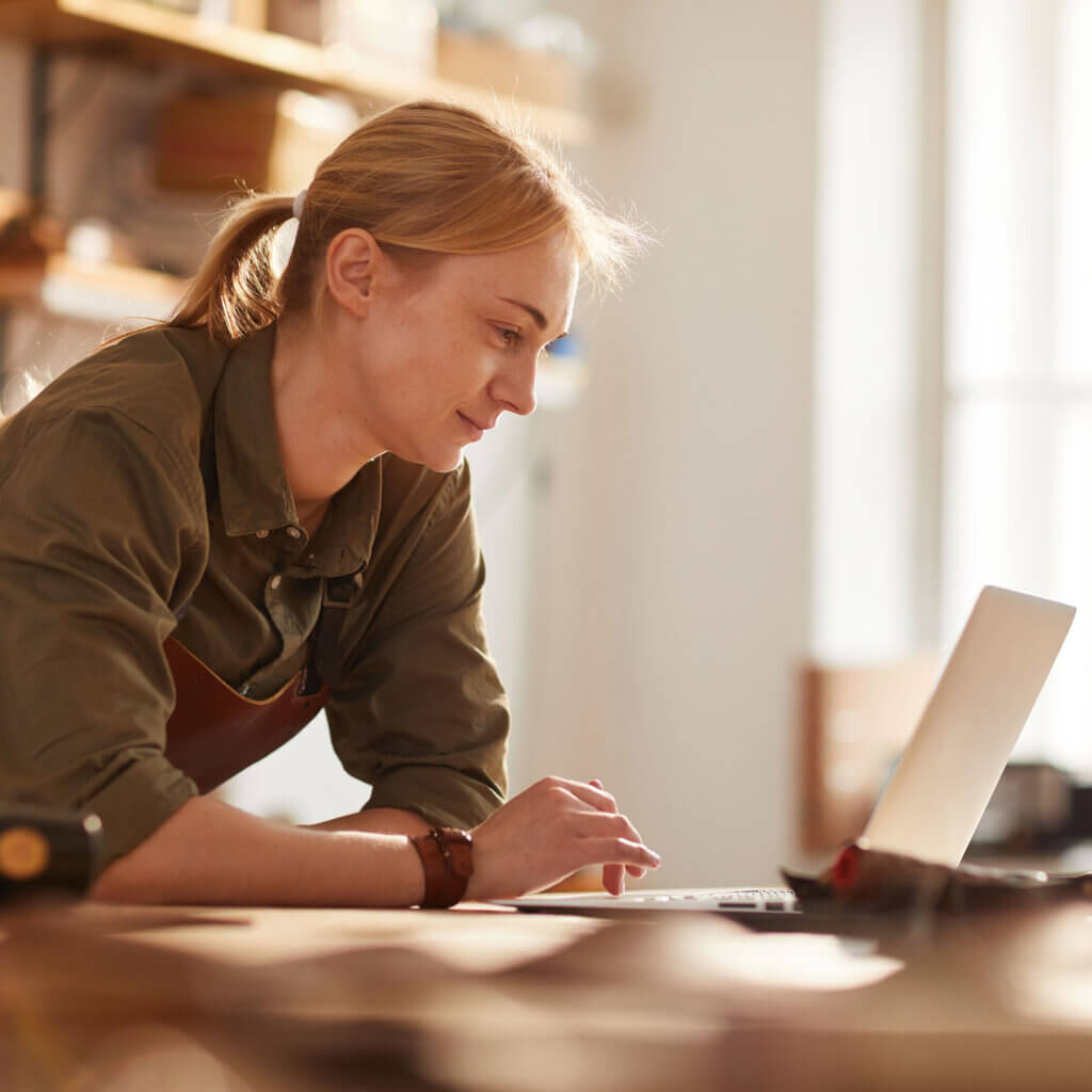 Female small business owner in crafting workshop looking at a laptop.