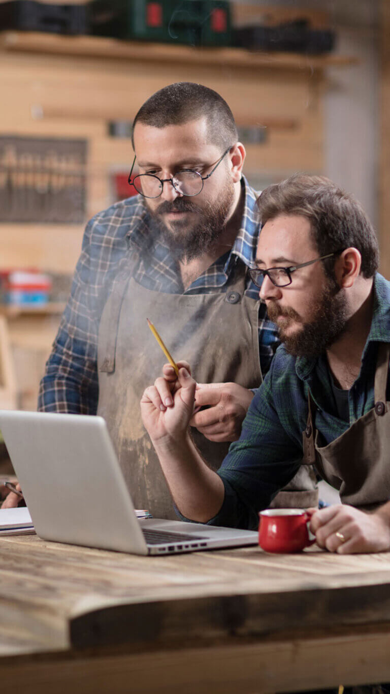 Two woodshop workers reviewing information on a laptop in their workshop.